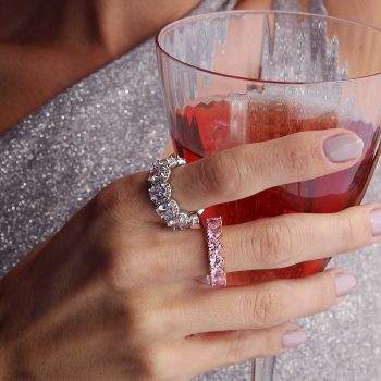 mujer con copa de vino y vestido brillante con anillos hernosos plateados con grandes cristales y uñas nude